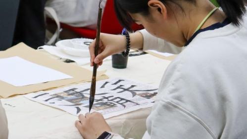 Student practicing calligraphy with a brush and ink during a cultural activity