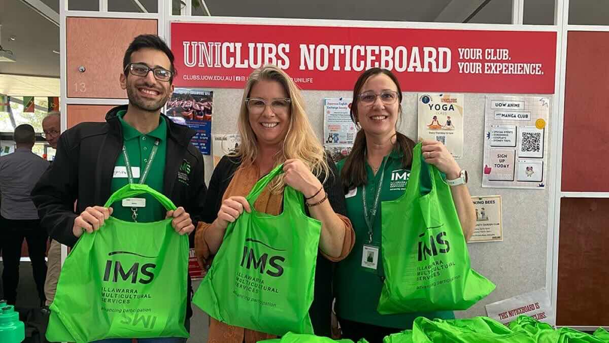 Three people holding Illawarra Multicultural Services merch and wearing IMS shirts